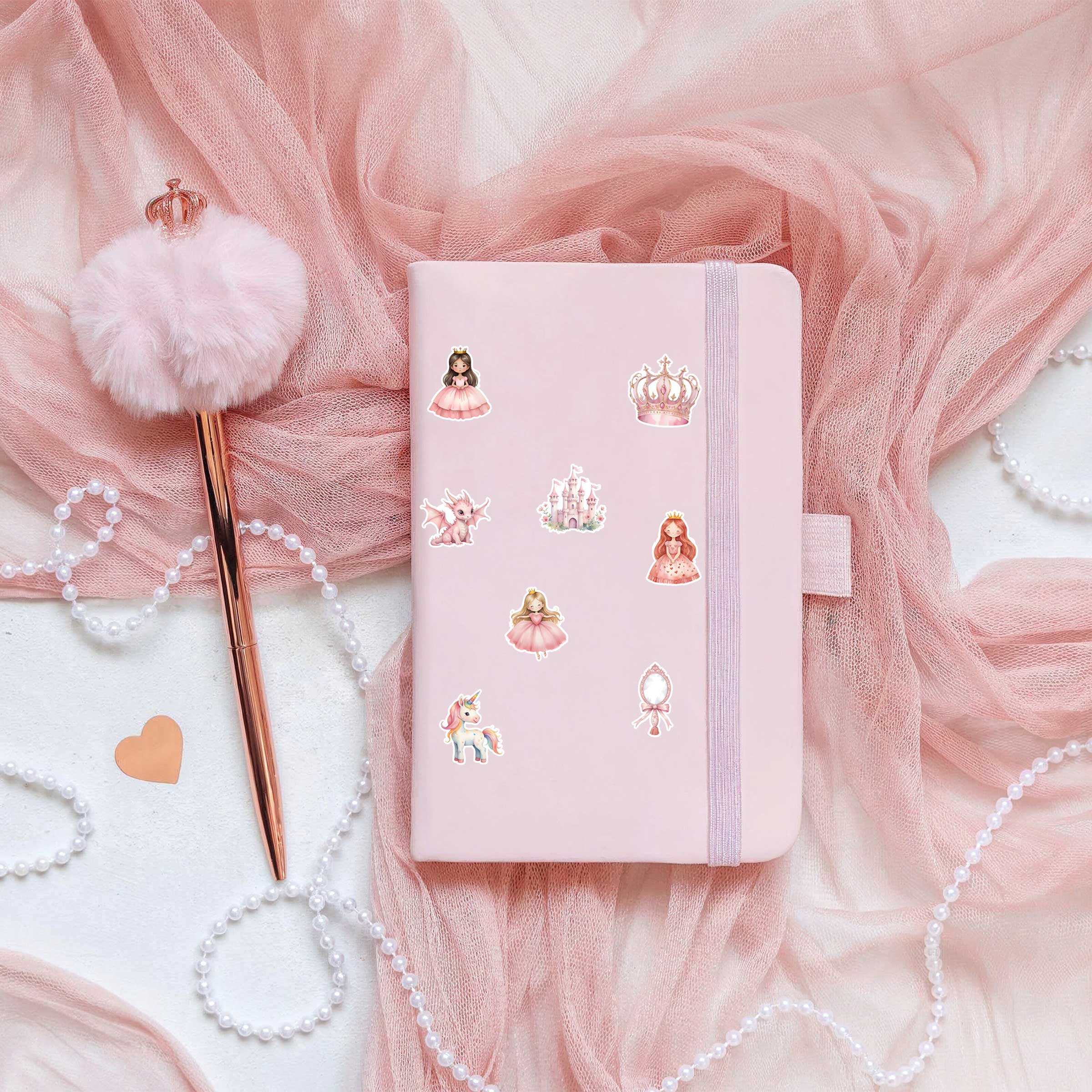 Roze notitieboek met prinsessenstickers erop, liggend op zachte roze tule met een pluizige roze pen ernaast.