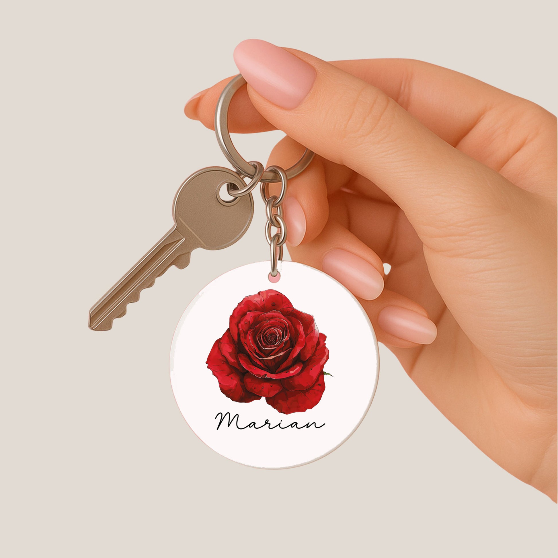 Ronde sleutelhanger met een rode roos en de naam Marian hangt aan een metalen sleutel met een hand op een beige achtergrond.