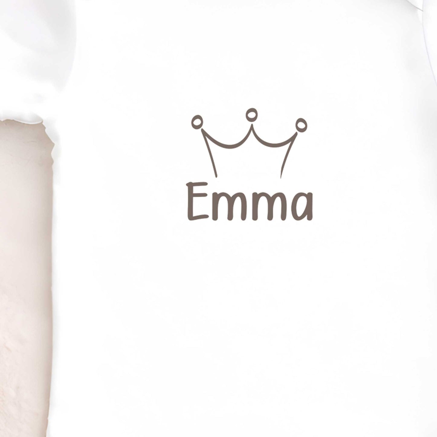 Close-up van een witte babyromper met een kroontje en de naam Emma op de voorkant.