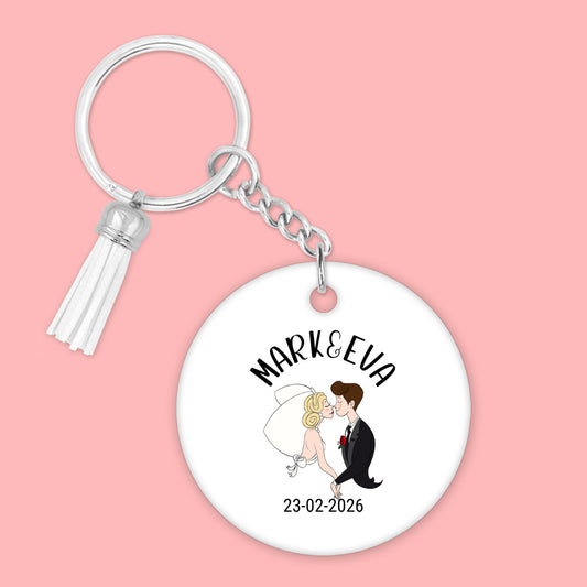 gepersonaliseerde slutelhanger voor bruispaar met namen en trouwdatum en een illustratie in de vorm van een cartoon bruilofststel. Aan de hanger hangt een wit suede kwastje