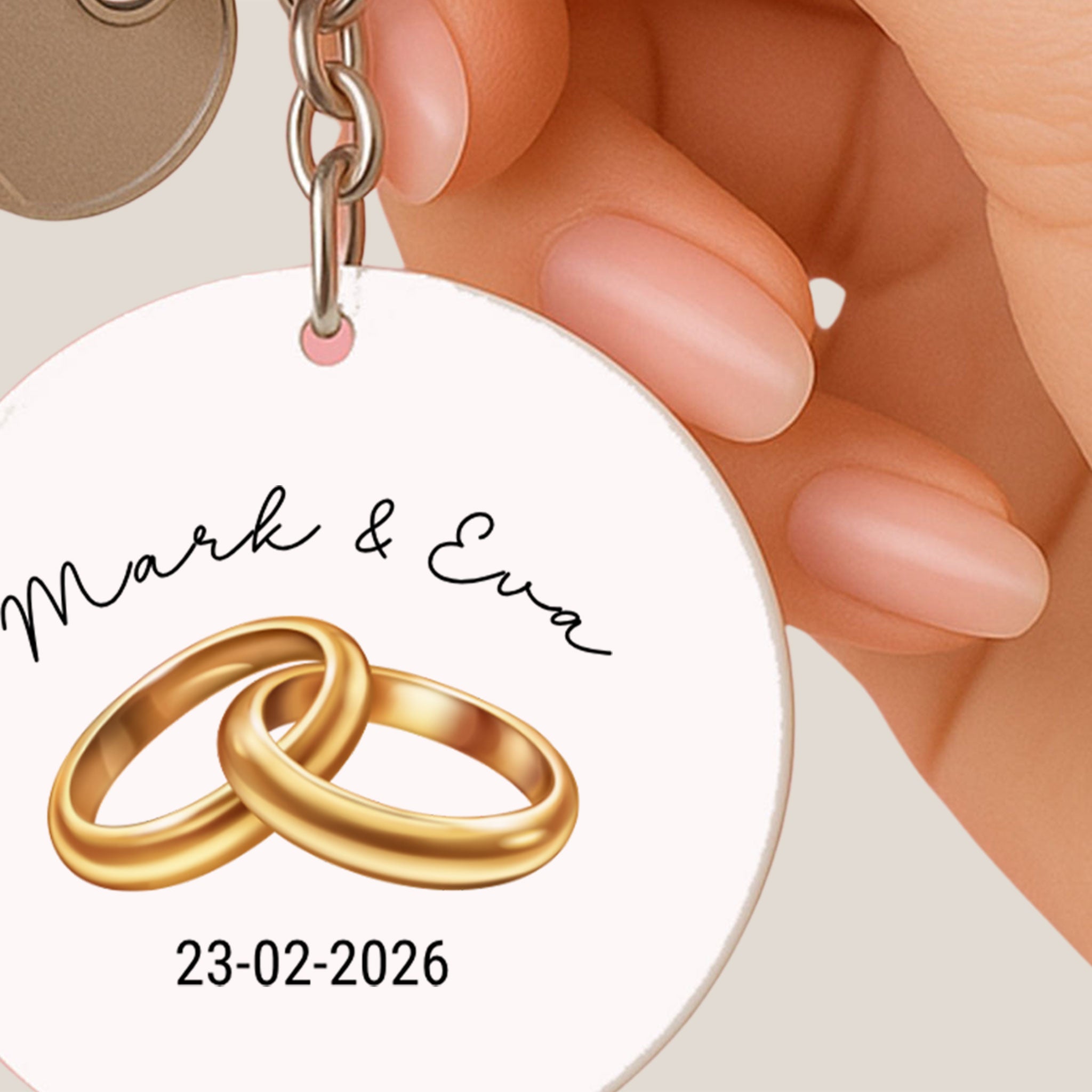 closeup van vrouwenhand  met witte ronde sleutelhanger met illustratie van 2 gouden trouwringen , namen van het aanstaande echtpaar en hun trouwdatum, tevens sleutel aan de sleutel ring