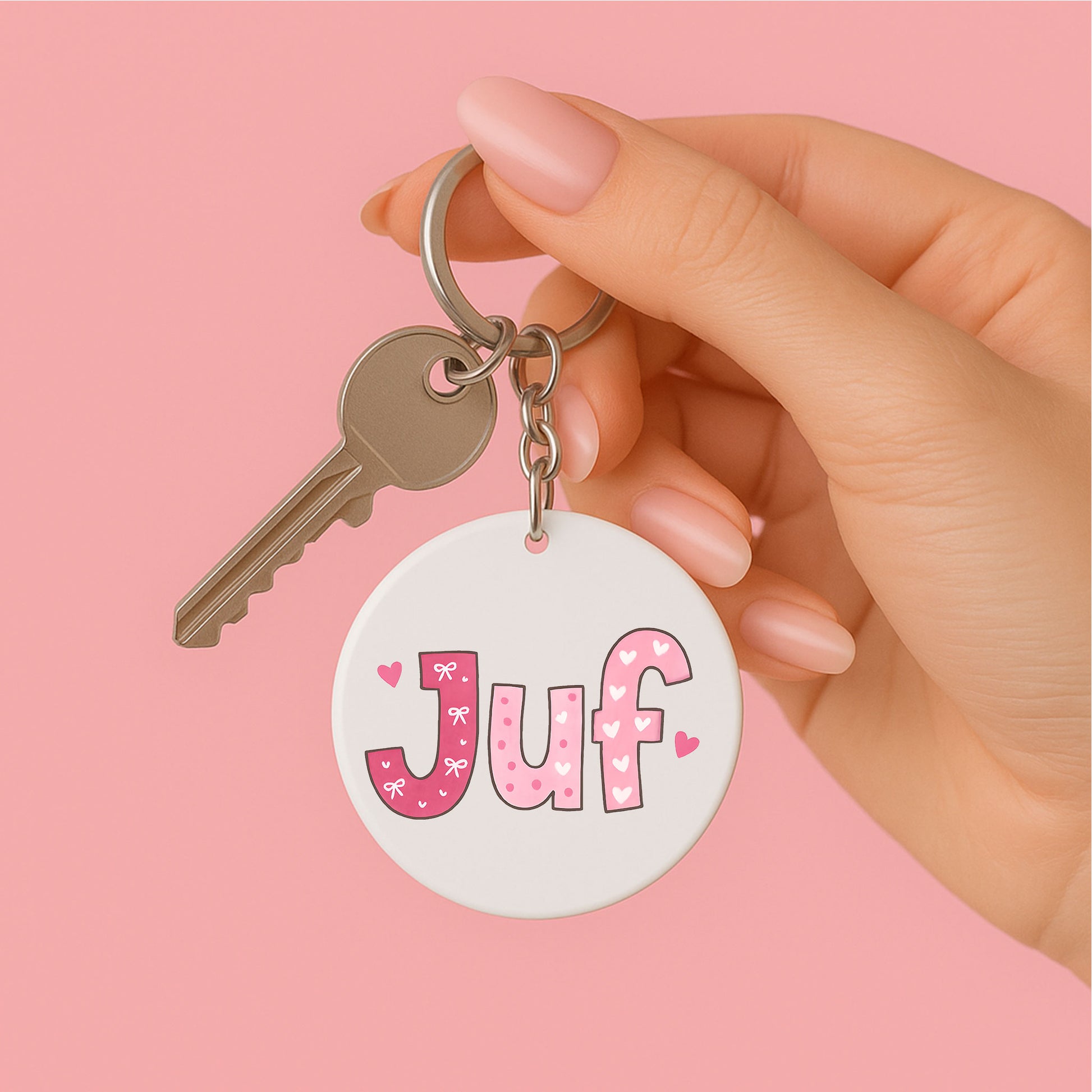 een vrouwen hand die een ronde sleutelhanger JUF roze met kwastje vasthoud