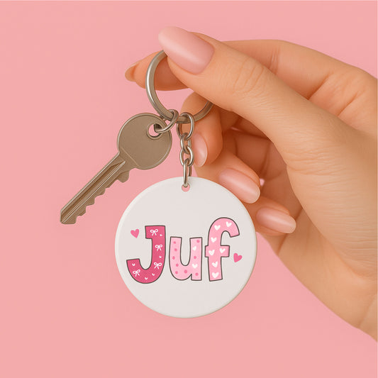 een vrouwen hand die een ronde sleutelhanger JUF roze met kwastje vasthoud