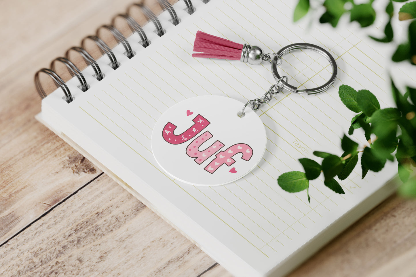 een ronde sleutelhanger JUF roze met kwastje op een notiteboek