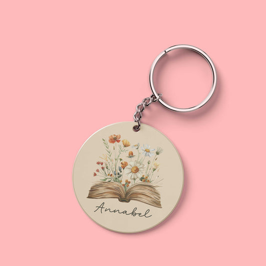 Ronde sleutelhanger met naam Annabel en illustratie van bloemen die uit open boek groeien.
