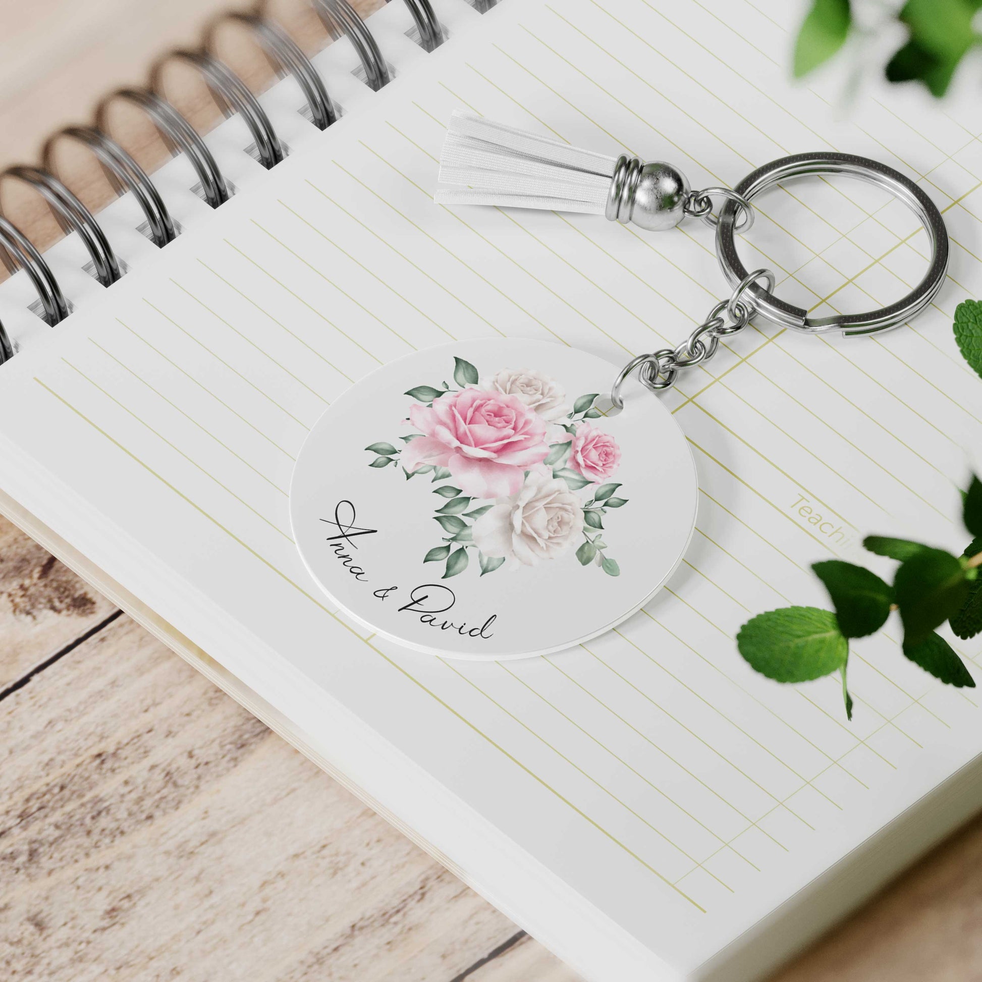 Gepersonaliseerde sleutelhanger met rozenillustratie en namen Anna & David, met wit suède kwastje op notitieboek