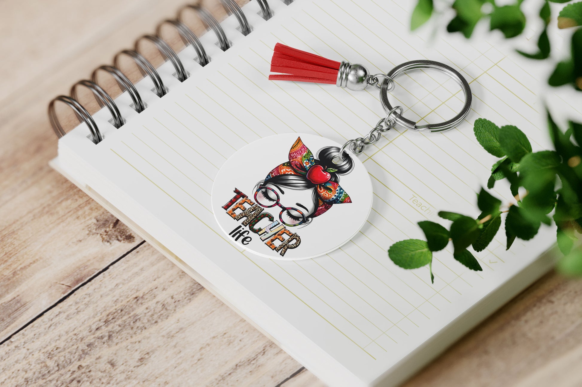 sleutelhanger met rood kwastje met een illustratie van een vrouw met bril en strik in haar haar en een tekst teacher life in bonte patronen op een notitieboek