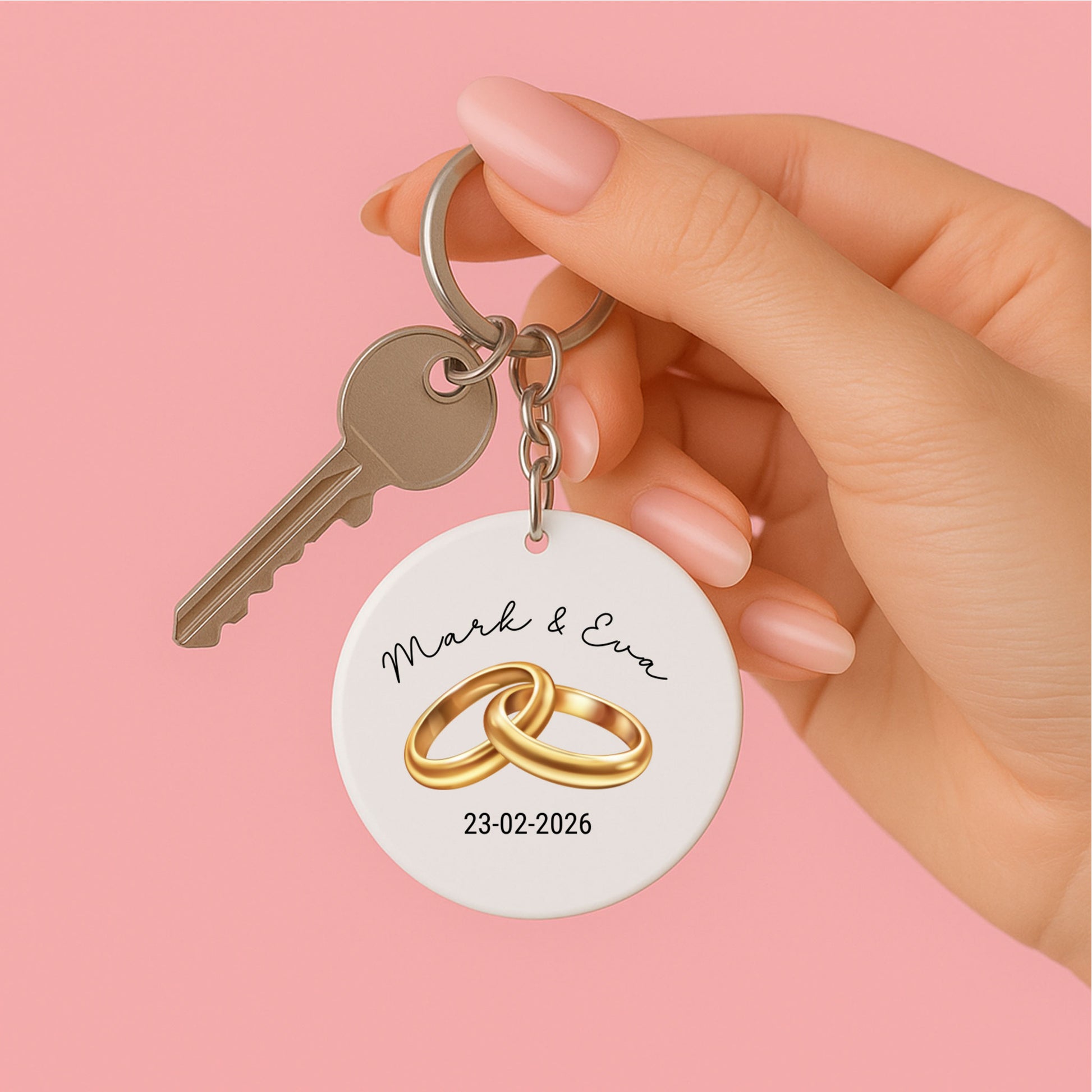 vrouwenhand  met witte ronde sleutelhanger met illustratie van 2 gouden trouwringen , namen van het aanstaande echtpaar en hun trouwdatum, tevens sleutel aan de sleutel ring
