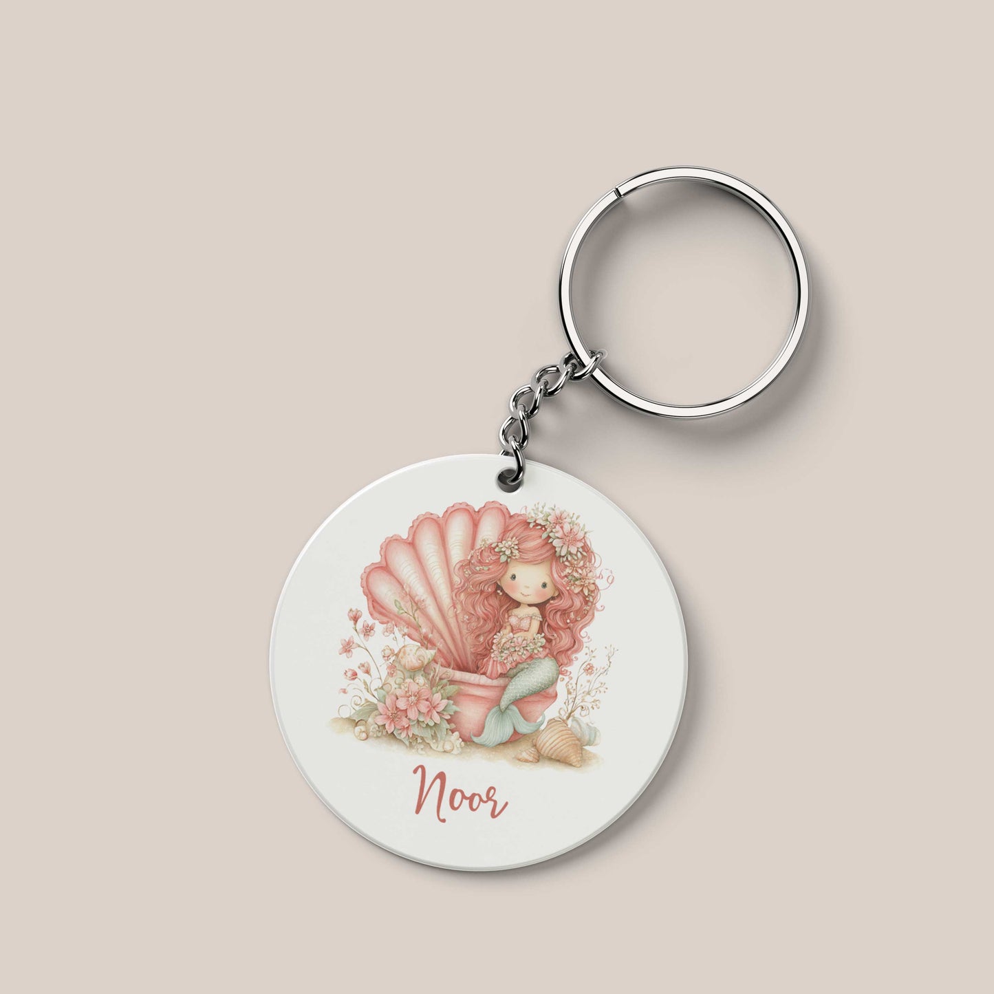Ronde gepersonaliseerde sleutelhanger met de naam Noor. Op de sleutelhanger staat een roze zeemeermin met lang krullend haar die in een grote roze schelp zit. Rondom haar staan bloemen, schelpen en zachte pastelaccenten.