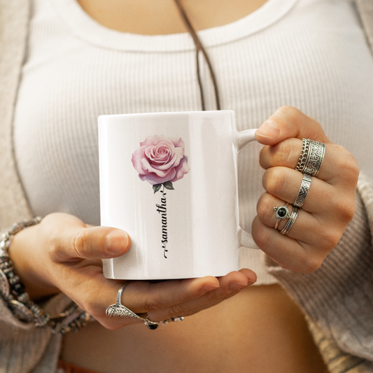 een vrouw die een mok vasthoud met daarop een roze roos en haar naam in de vorm van de stam van de roos in sierlijke letters
