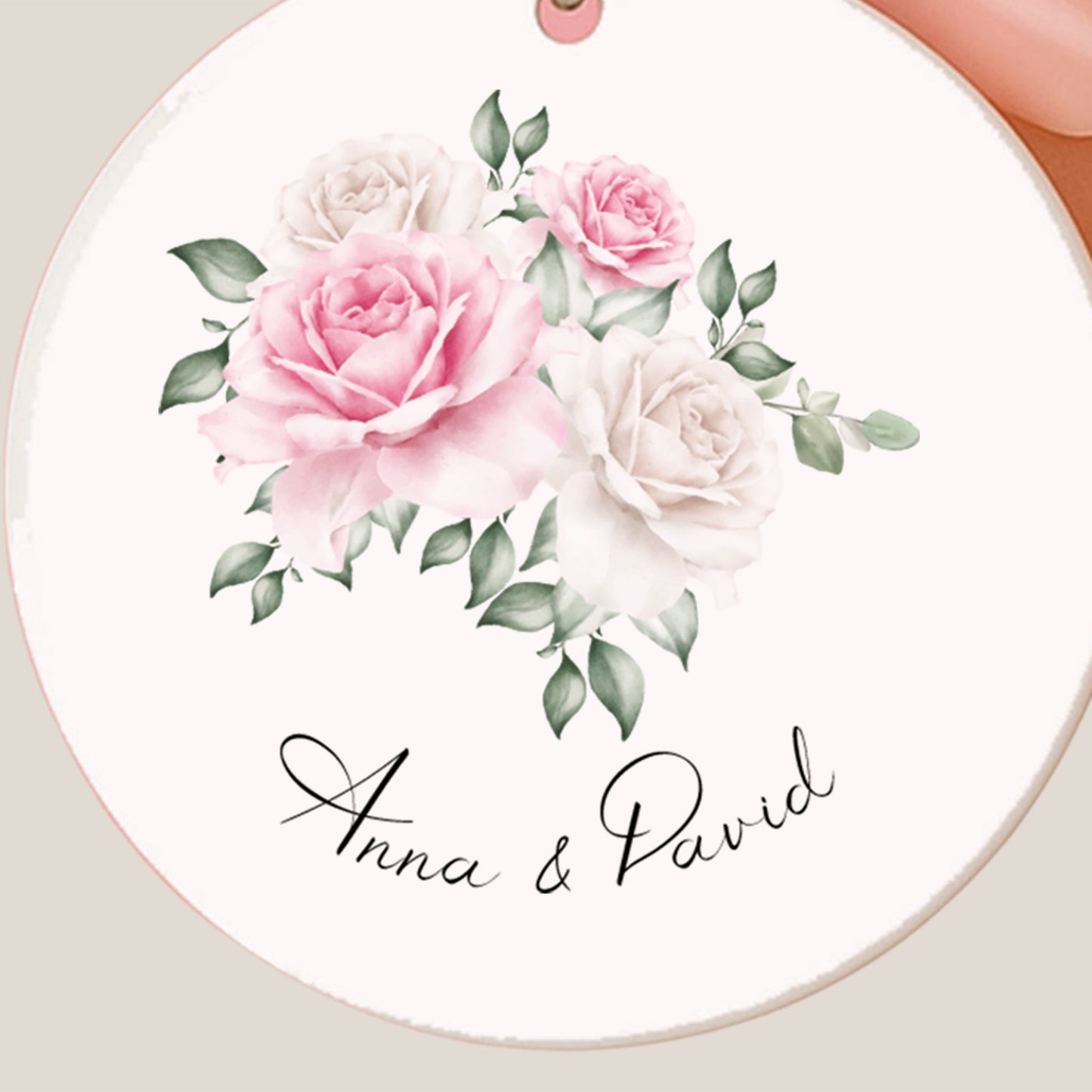 Close-up van de ronde sleutelhanger met roze en witte bloemenillustratie en de namen van het bruidspaar.