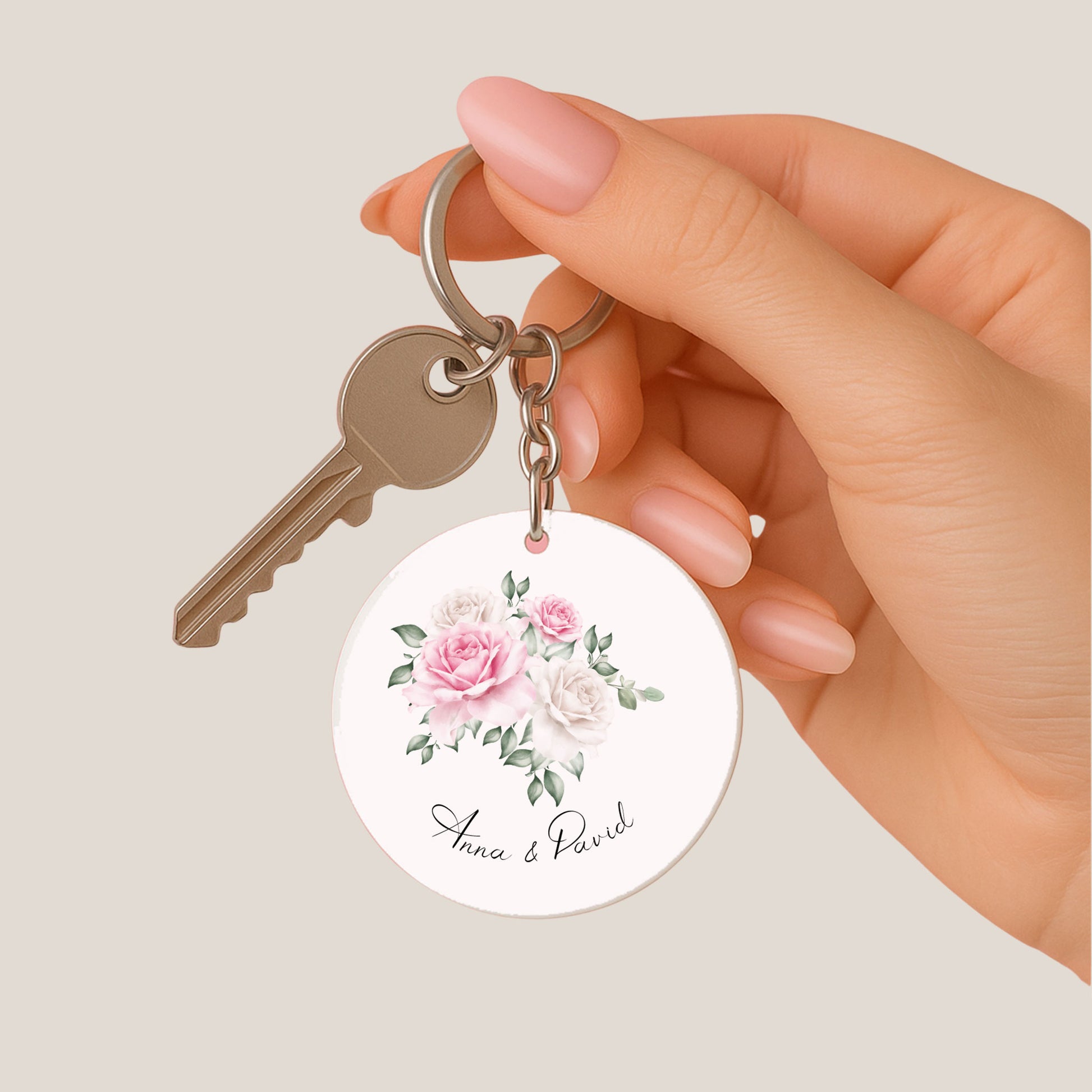 Hand houdt een sleutel met daaraan een ronde sleutelhanger met bloemenillustratie en de namen van het bruidspaar.