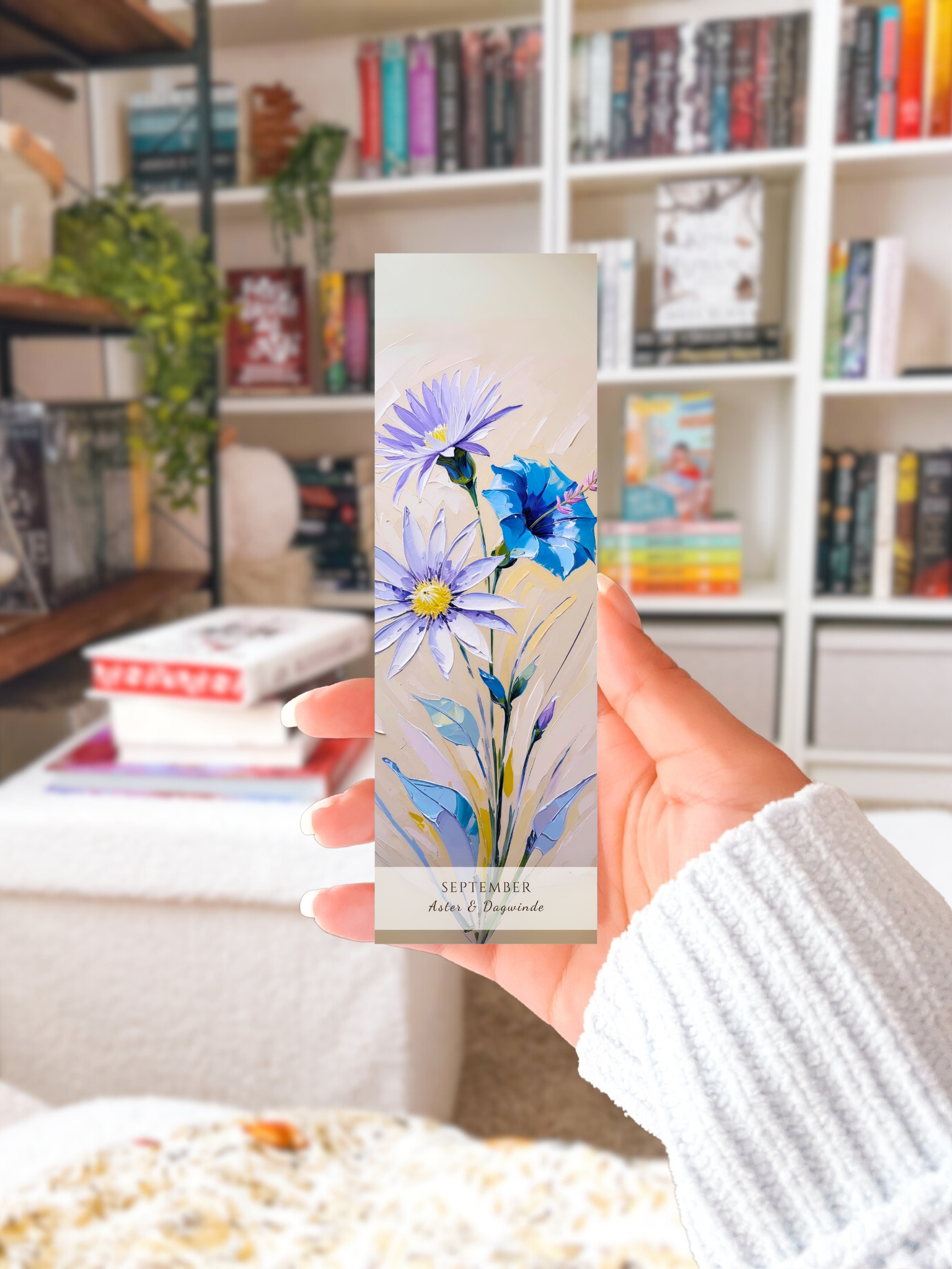 vrouw met bookmark in haar hand in haar woonkamer voor haar boekenkast. Geboorte bloem boekenlegger voor de maand september, met  kunstzinnige illustratie van Aster & Dagwinde.