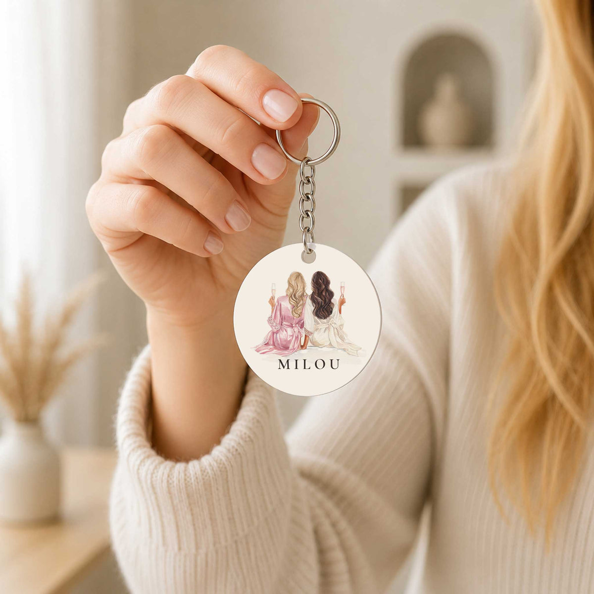 Vrouw houdt een ronde sleutelhanger vast met een illustratie van twee vrouwen en de naam Milou