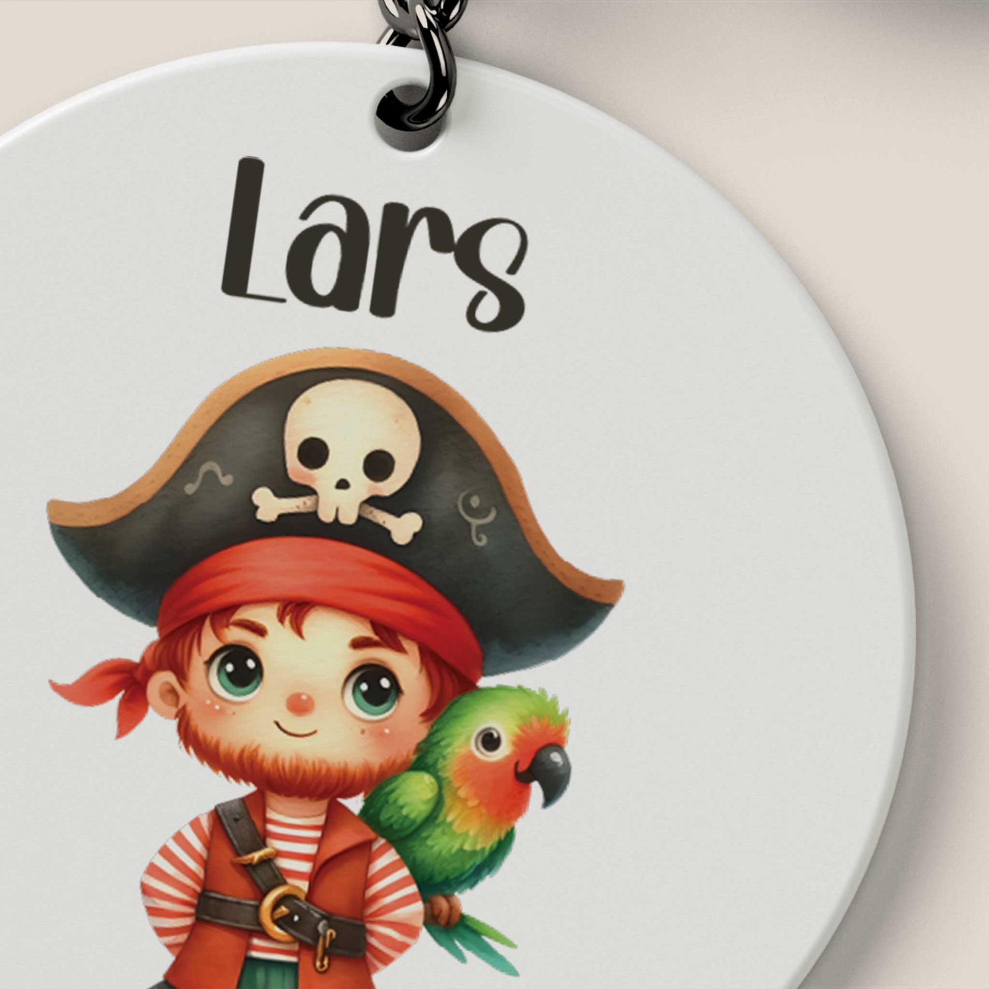 Close-up van een ronde witte sleutelhanger met de naam Lars en een piraatje met een papegaai op zijn schouder.