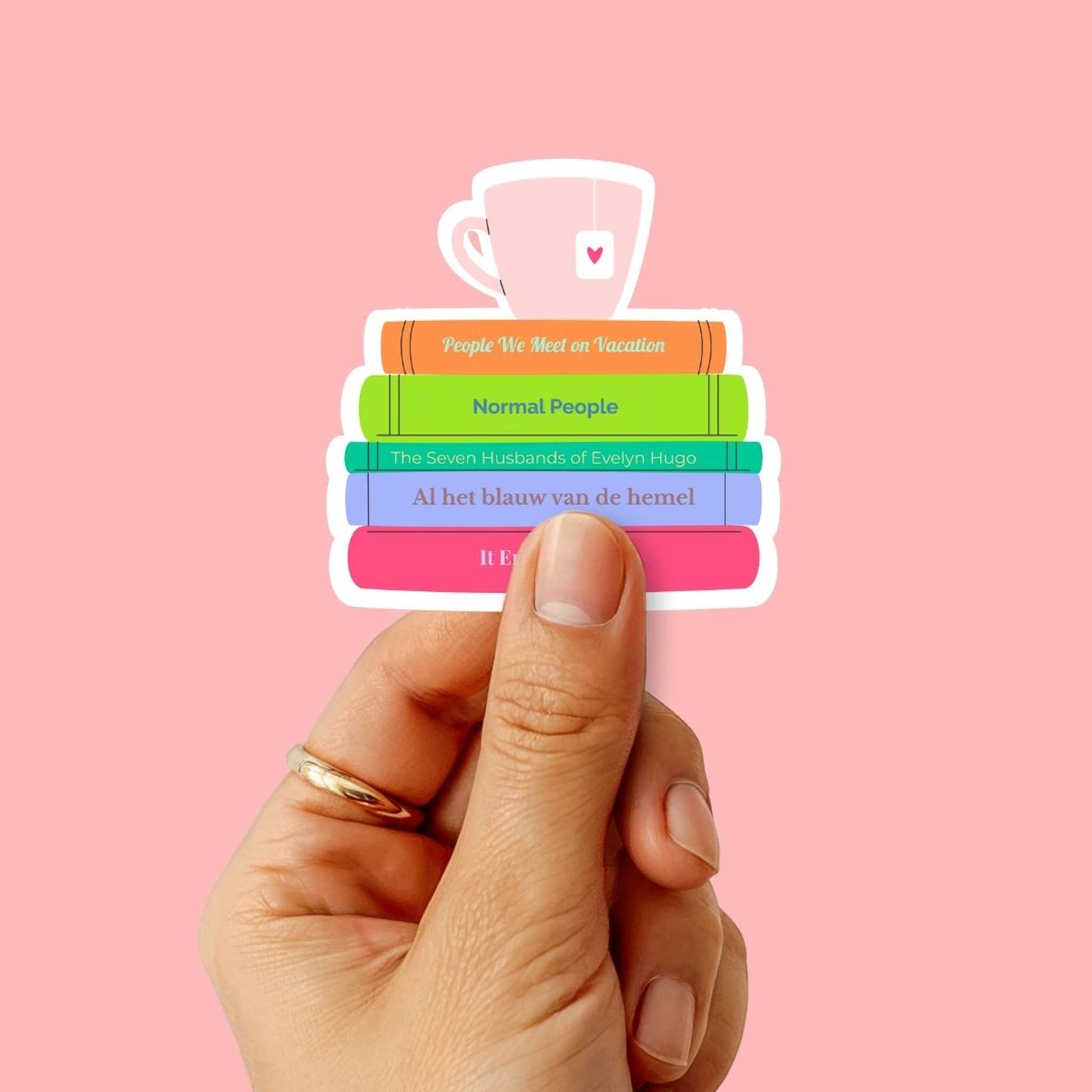 Sticker van een kleurrijke boekenstapel met populaire titels, vastgehouden in een hand op een roze achtergrond