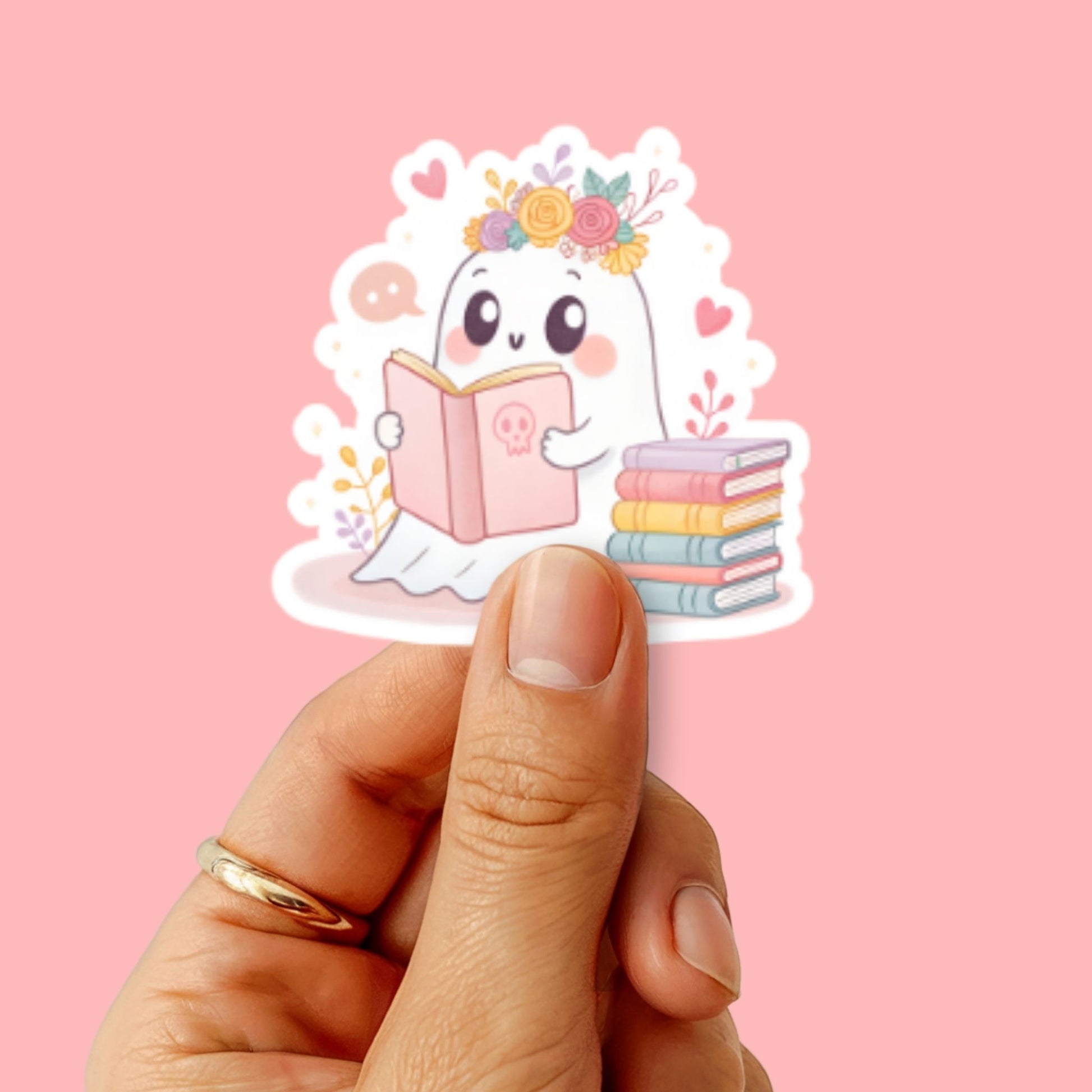 Sticker met lezend spookje wordt vastgehouden door een hand met roze achtergrond, goed zichtbare details van het ontwerp.