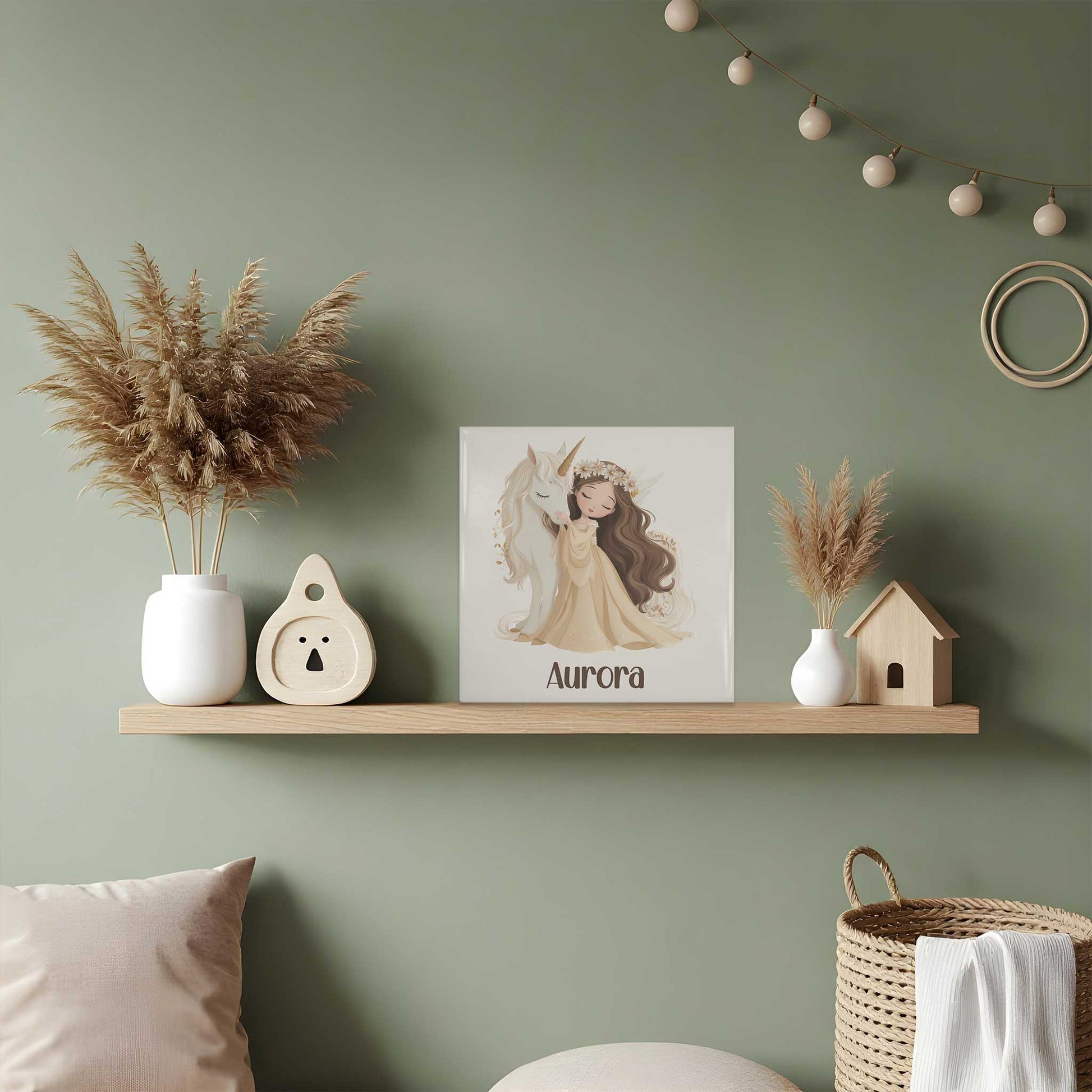 Keramisch tegeltje met een illustratie van een prinses die een witte eenhoorn omhelst. Onder de illustratie staat de naam Aurora. Het tegeltje staat op een houten plank in een kinderkamer tussen droogbloemen en houten decoratie.