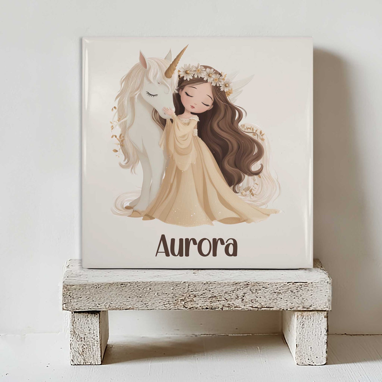 Keramisch tegeltje met een prinses die een witte eenhoorn omhelst en de naam Aurora. Het tegeltje staat op een wit houten krukje tegen een lichte muur.