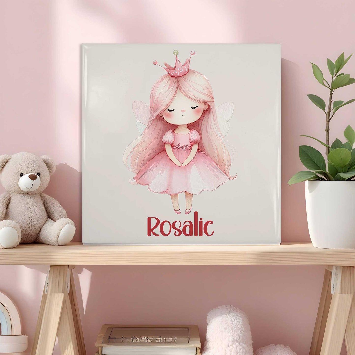 Keramisch tegeltje met een prinses met roze haar, een roze jurk en een kroontje. Onder de illustratie staat de naam Rosalie. Het tegeltje staat op een houten plank in een roze kinderkamer naast een knuffelbeer en een plant.
