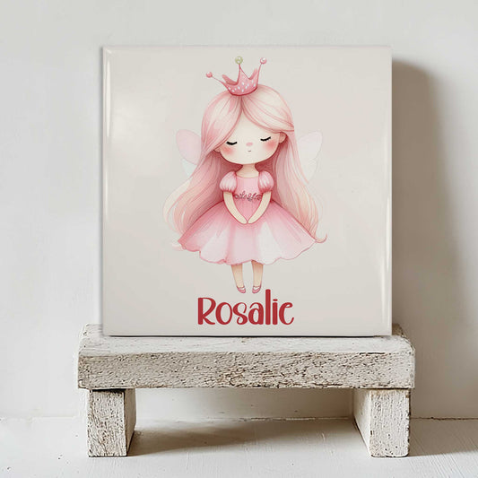 Keramisch tegeltje met een schattige prinses met lang roze haar, een roze kroontje en kleine vleugeltjes. Onder de illustratie staat de naam Rosalie. Het tegeltje staat op een wit houten krukje.