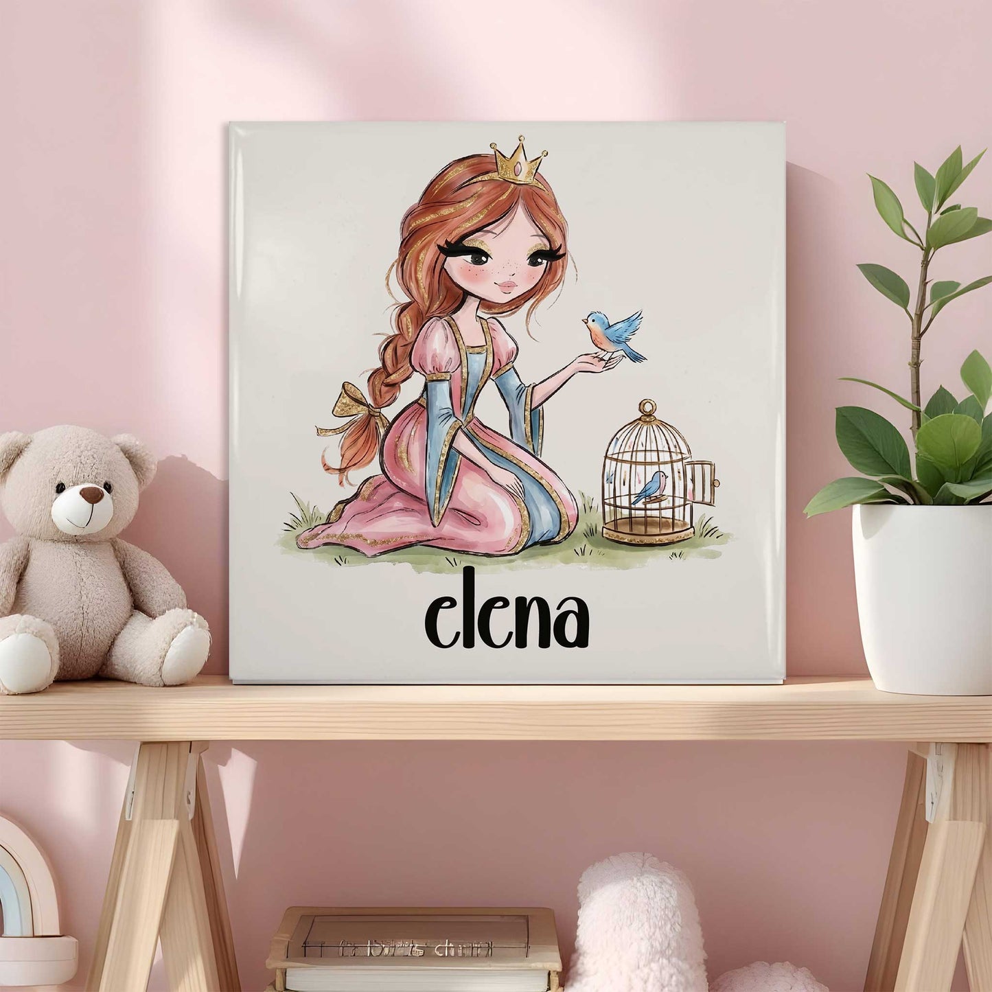 Keramisch tegeltje met een prinses in een roze jurk en gouden kroontje. Op haar hand zit een blauw vogeltje en naast haar staat een open vogelkooitje. Onder de illustratie staat de naam Elena. Het tegeltje staat op een houten plank in een roze kinderkamer naast een knuffelbeer en een plant.