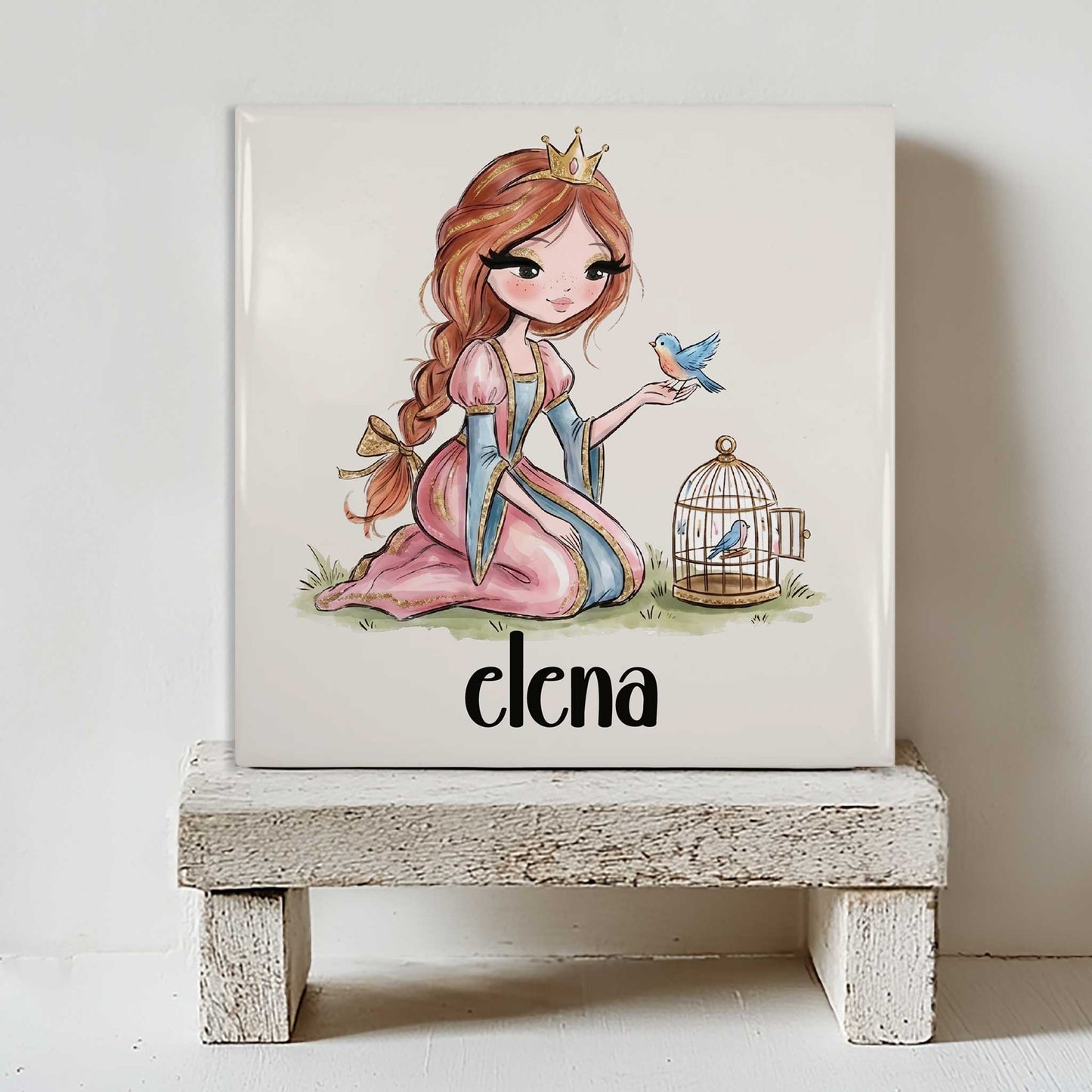 Keramisch tegeltje met een prinses in een roze jurk en gouden kroontje, een blauw vogeltje op haar hand en een open vogelkooitje. Onder de illustratie staat de naam Elena.