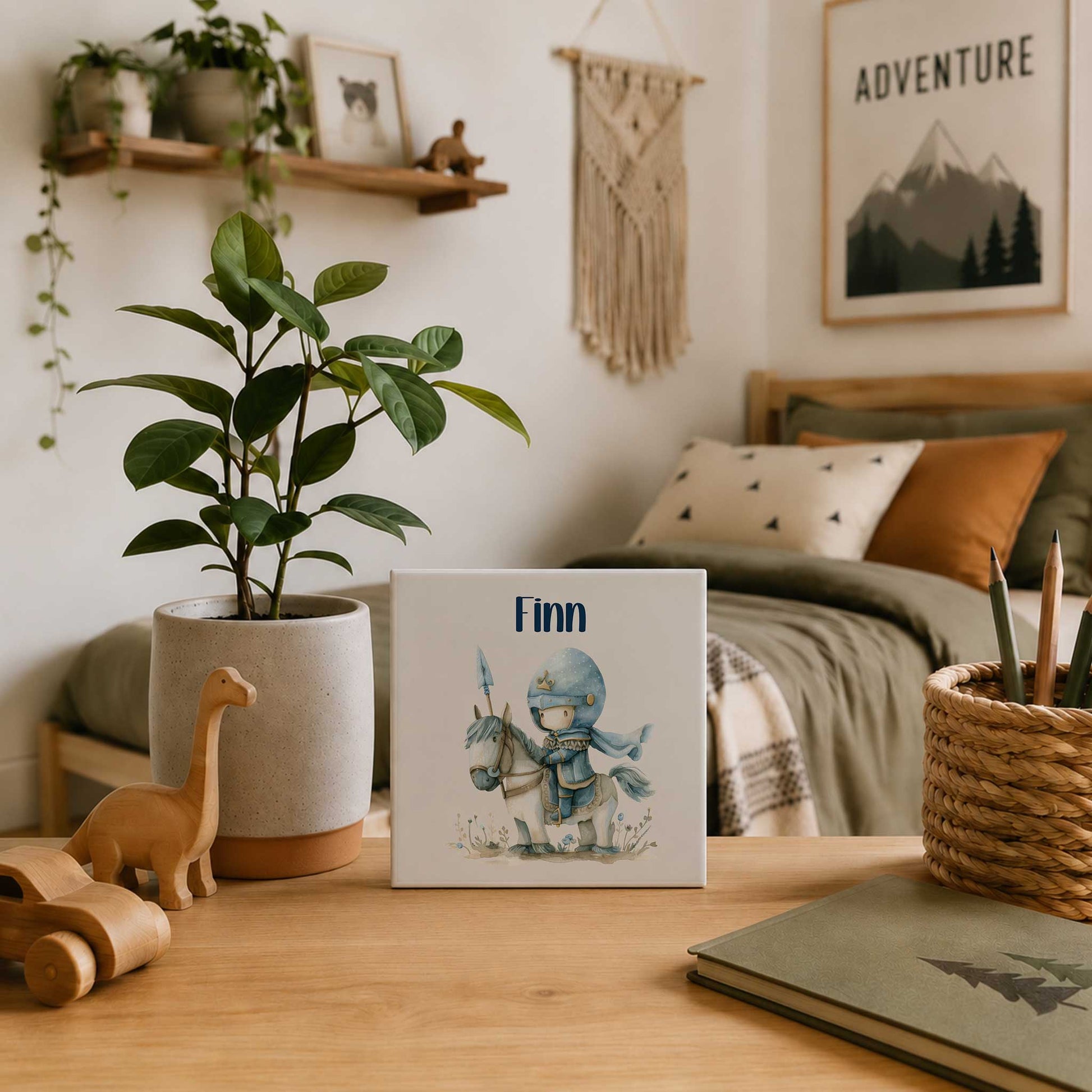 Keramieken tegeltje met de naam Finn en een illustratie van een kleine ridder op een wit paard op een houten bureau in een kinderkamer.