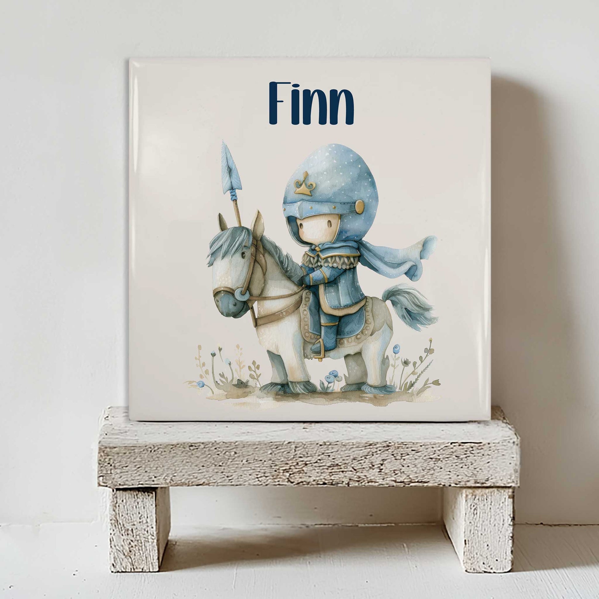 Keramiek tegeltje met de naam Finn en een illustratie van een kleine ridder op een wit paard op een wit houten krukje.