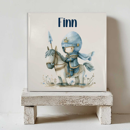 Keramiek tegeltje met de naam Finn en een illustratie van een kleine ridder op een wit paard op een wit houten krukje.