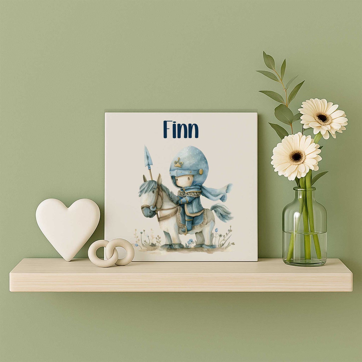 Keramieken tegeltje met de naam Finn en een illustratie van een kleine ridder op een wit paard op een houten wandplank naast een vaas met bloemen en decoratie.