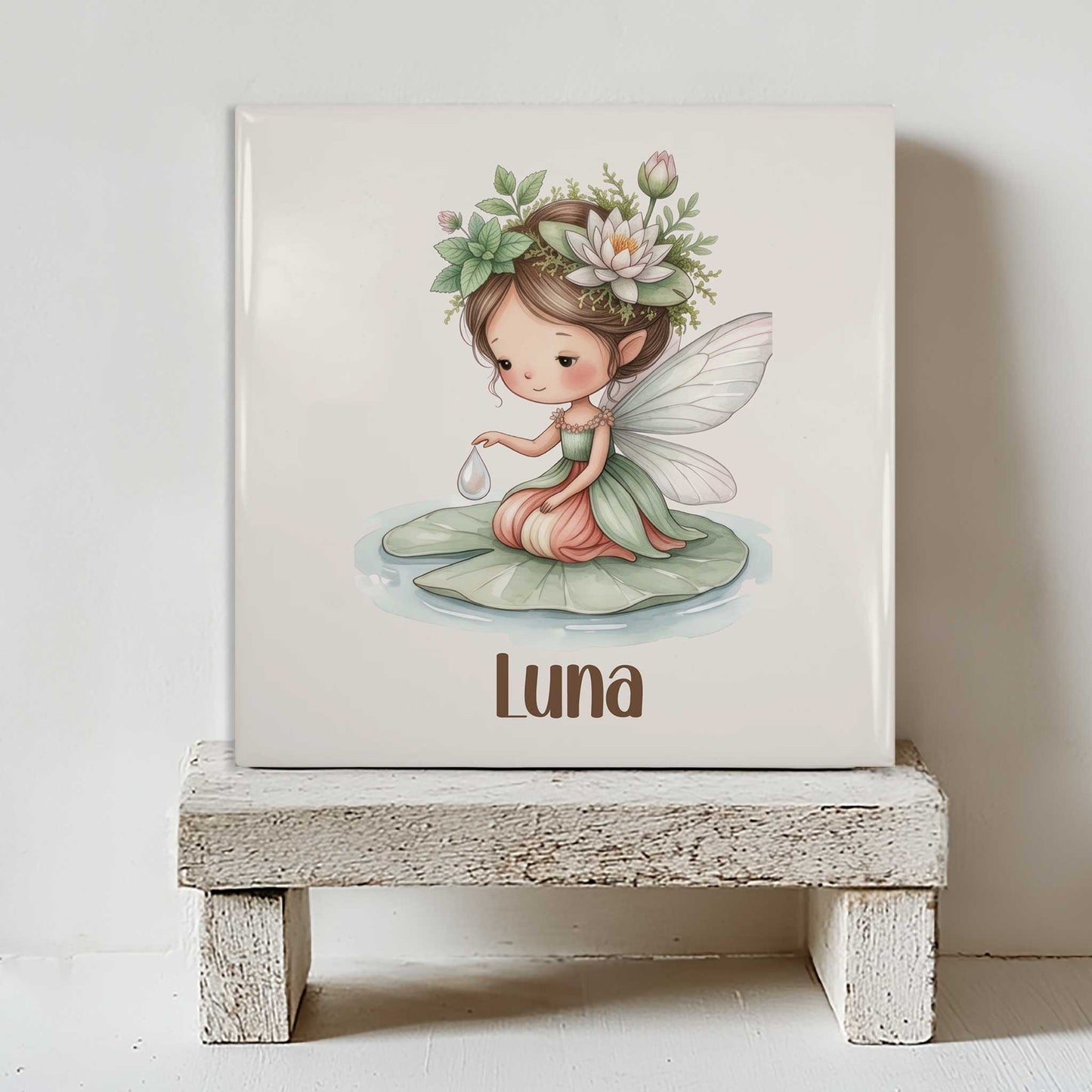 Keramisch tegeltje met naam Luna op een wit houten krukje met illustratie van een waterleliefee op een waterlelieblad.