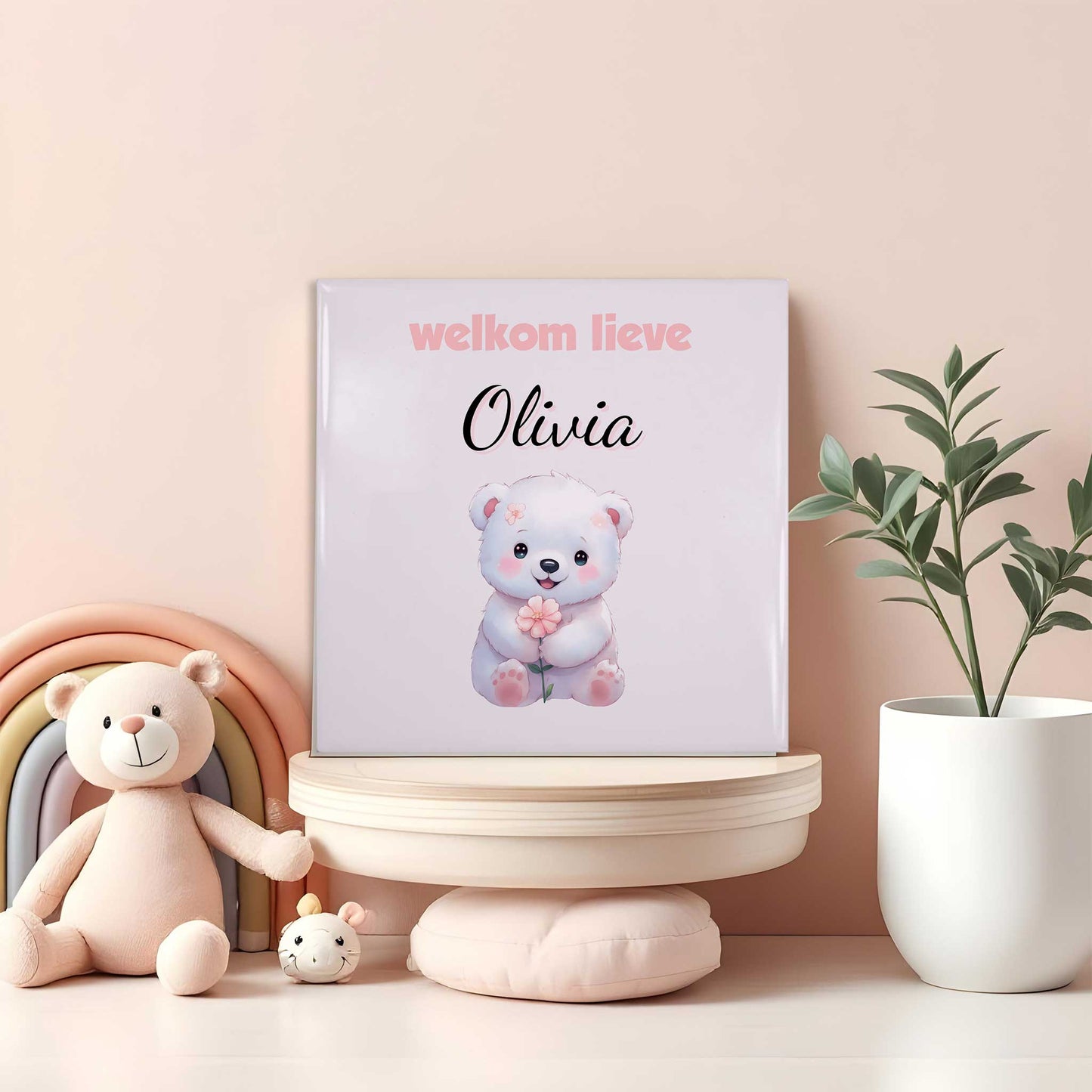 Babytegeltje met wit beertje, roze bloem en naam Olivia op plank tussen regenboog en knuffels