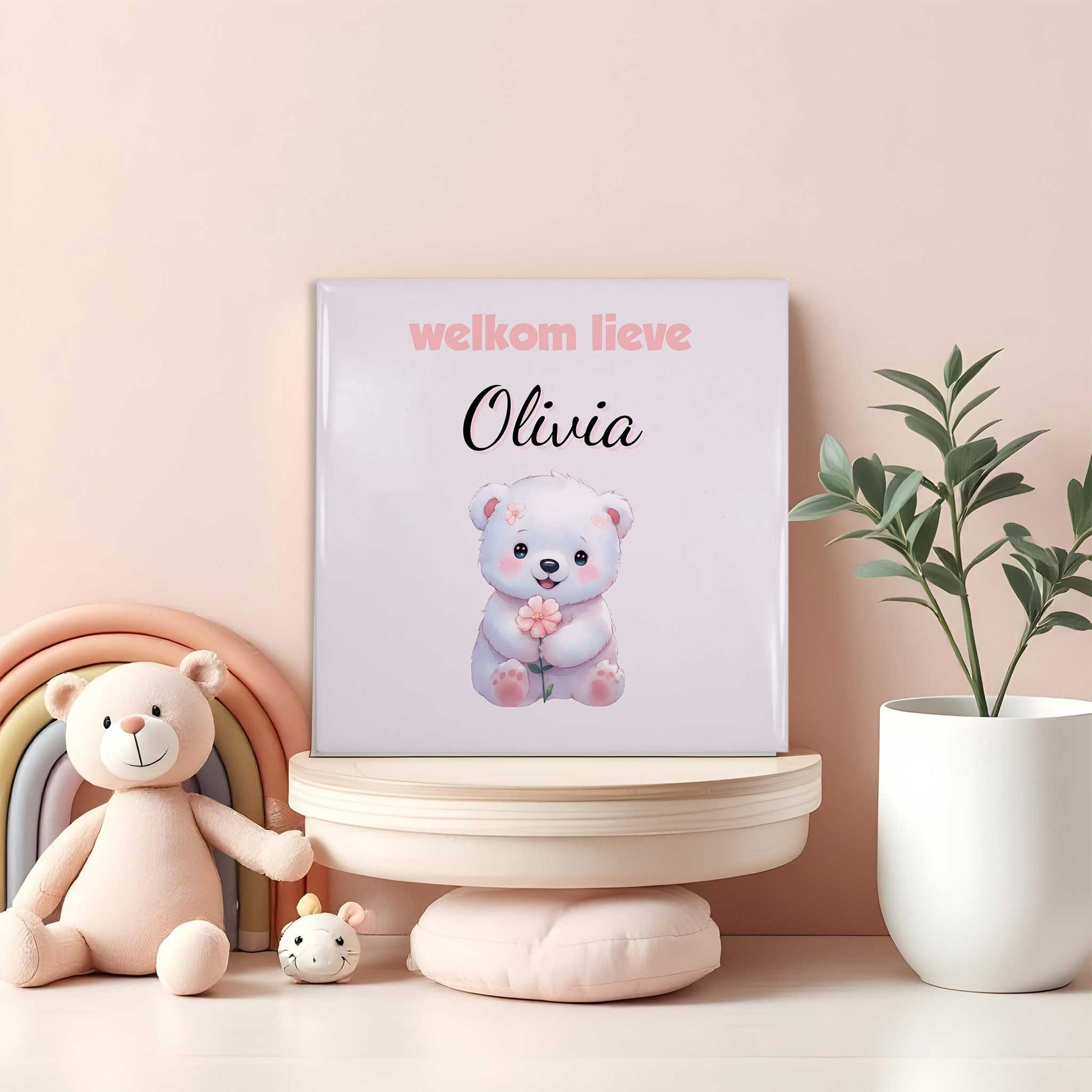 Babytegeltje met wit beertje, roze bloem en naam Olivia op plank tussen regenboog en knuffels