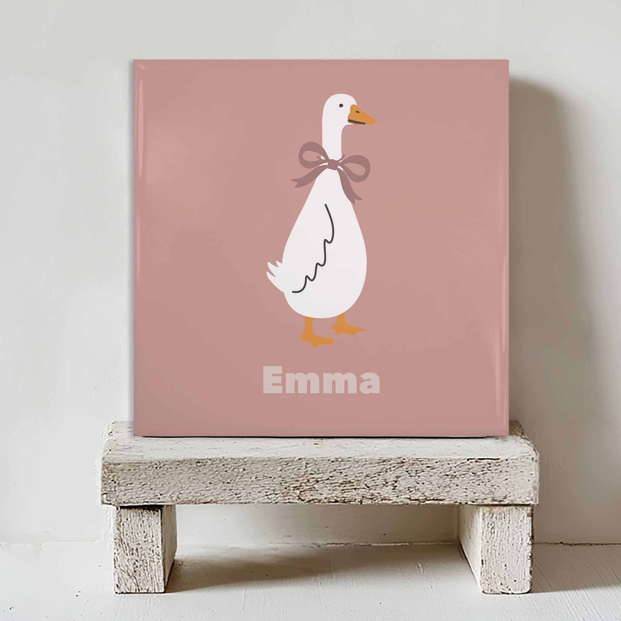 Gepersonaliseerd tegeltje met een illustratie van een gans en de naam Emma, geplaatst op een houten krukje