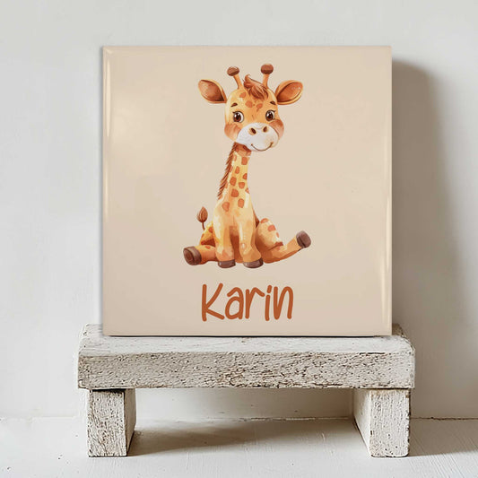 Keramisch tegeltje met een illustratie van een giraf en de naam Karin in beige tinten, geplaatst op een witte houten kruk