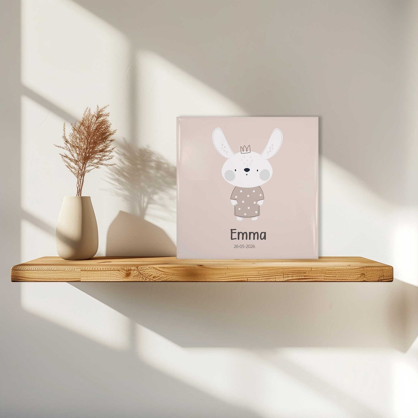 Keramisch geboortetegeltje met konijntje en naam Emma op houten wandplank met zacht daglicht en schaduw