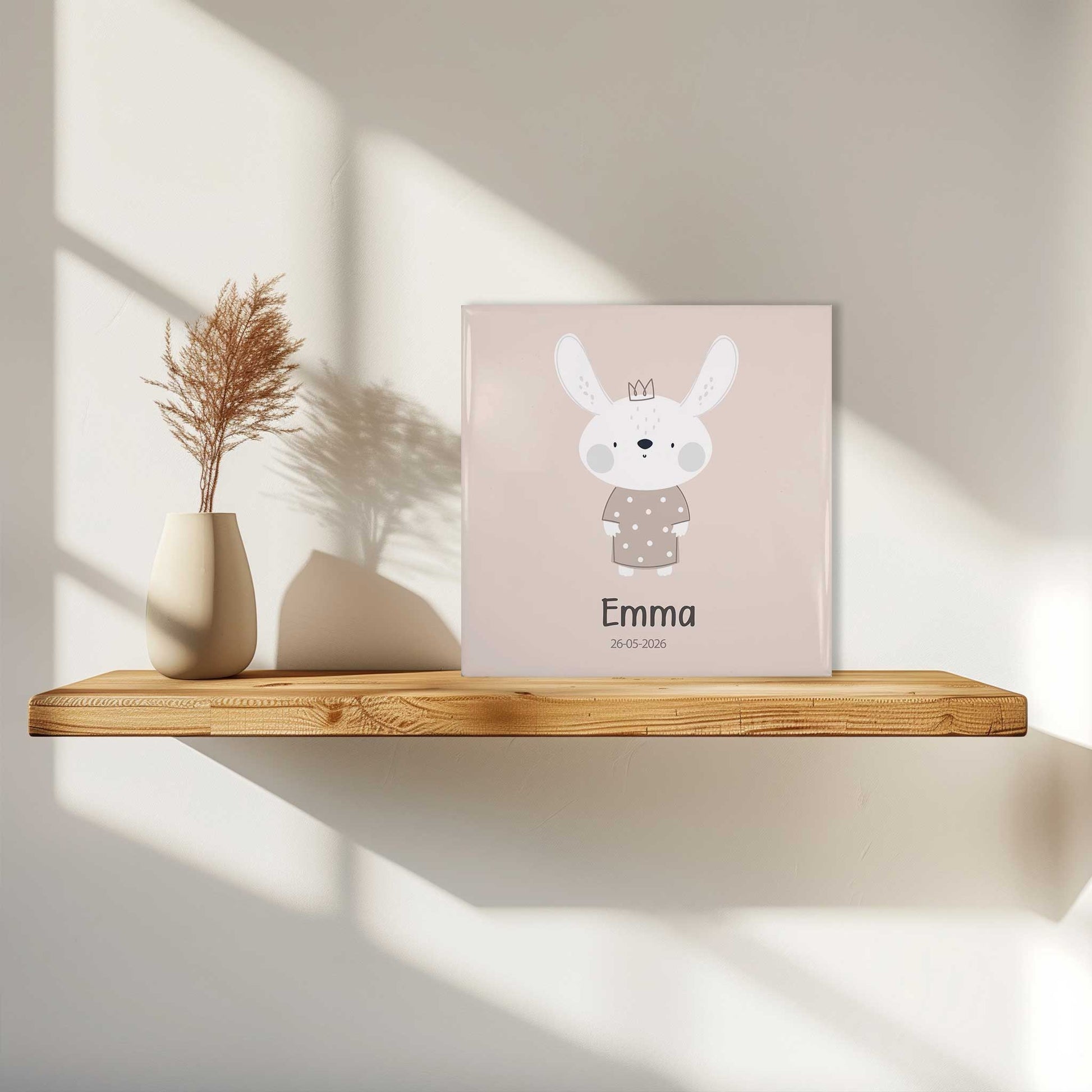 Keramisch geboortetegeltje met konijntje en naam Emma op houten wandplank met zacht daglicht en schaduw