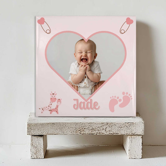 Keramisch tegeltje met een foto van een lachende baby in een hartvormig kader, met de naam Jade eronder, geplaatst op een witte houten kruk