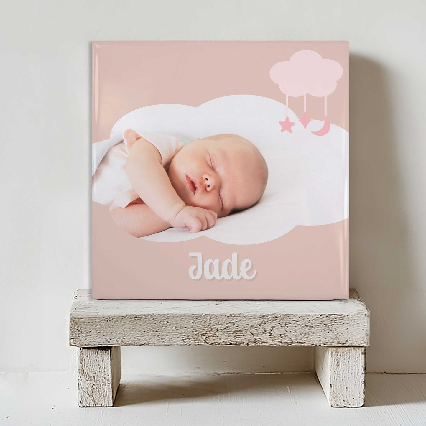 Keramisch tegeltje met een foto van een slapende baby in een wolkvormig kader, met de naam Jade eronder, geplaatst op een witte houten kruk
