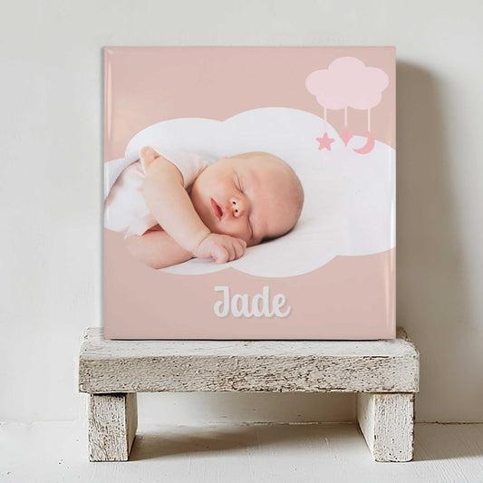 Keramisch tegeltje met een foto van een slapende baby in een wolkvormig kader, met de naam Jade eronder, geplaatst op een witte houten kruk