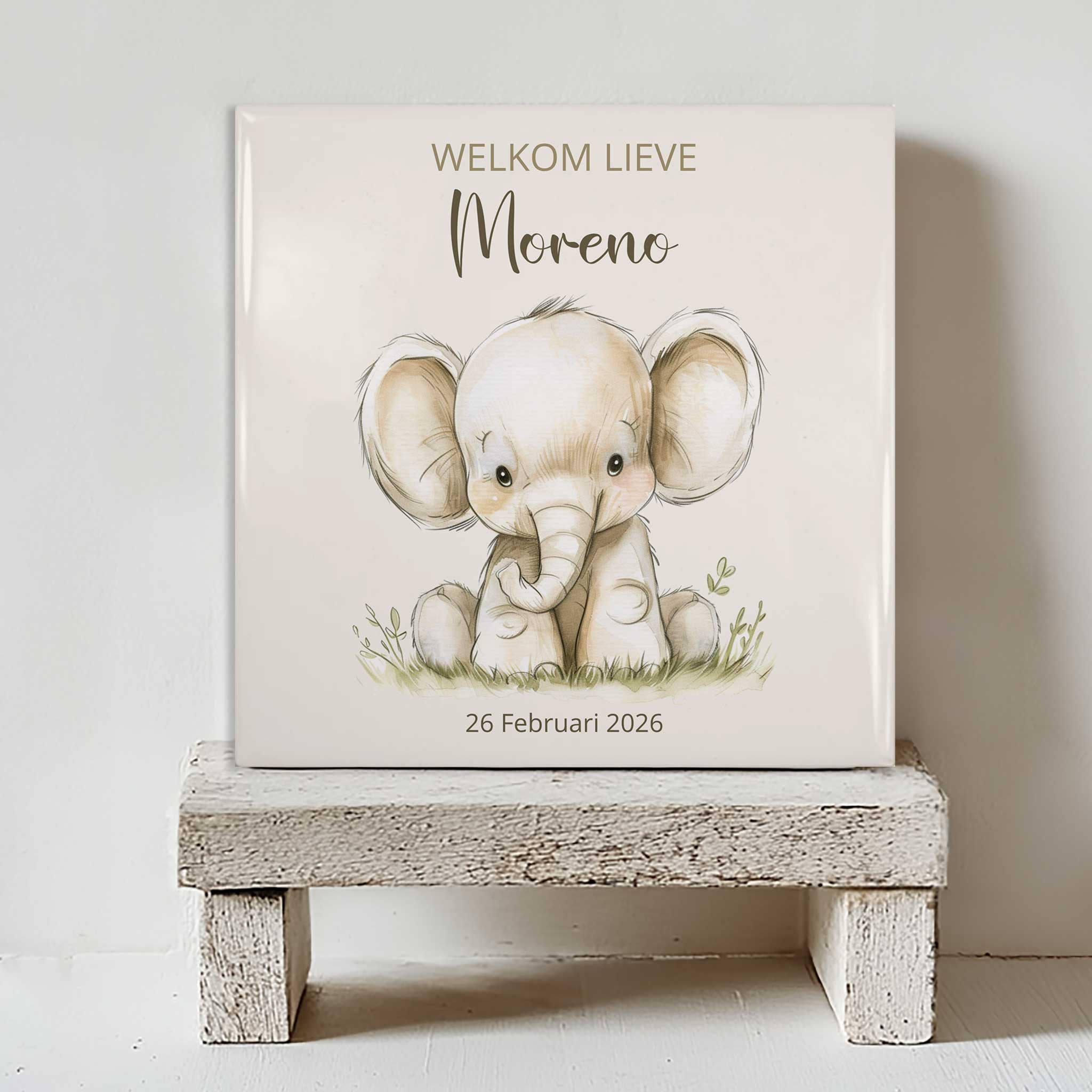Keramisch tegeltje met een illustratie van een olifant, de tekst “welkom lieve Moreno” en de datum 26 februari 2026, geplaatst op een witte houten kruk