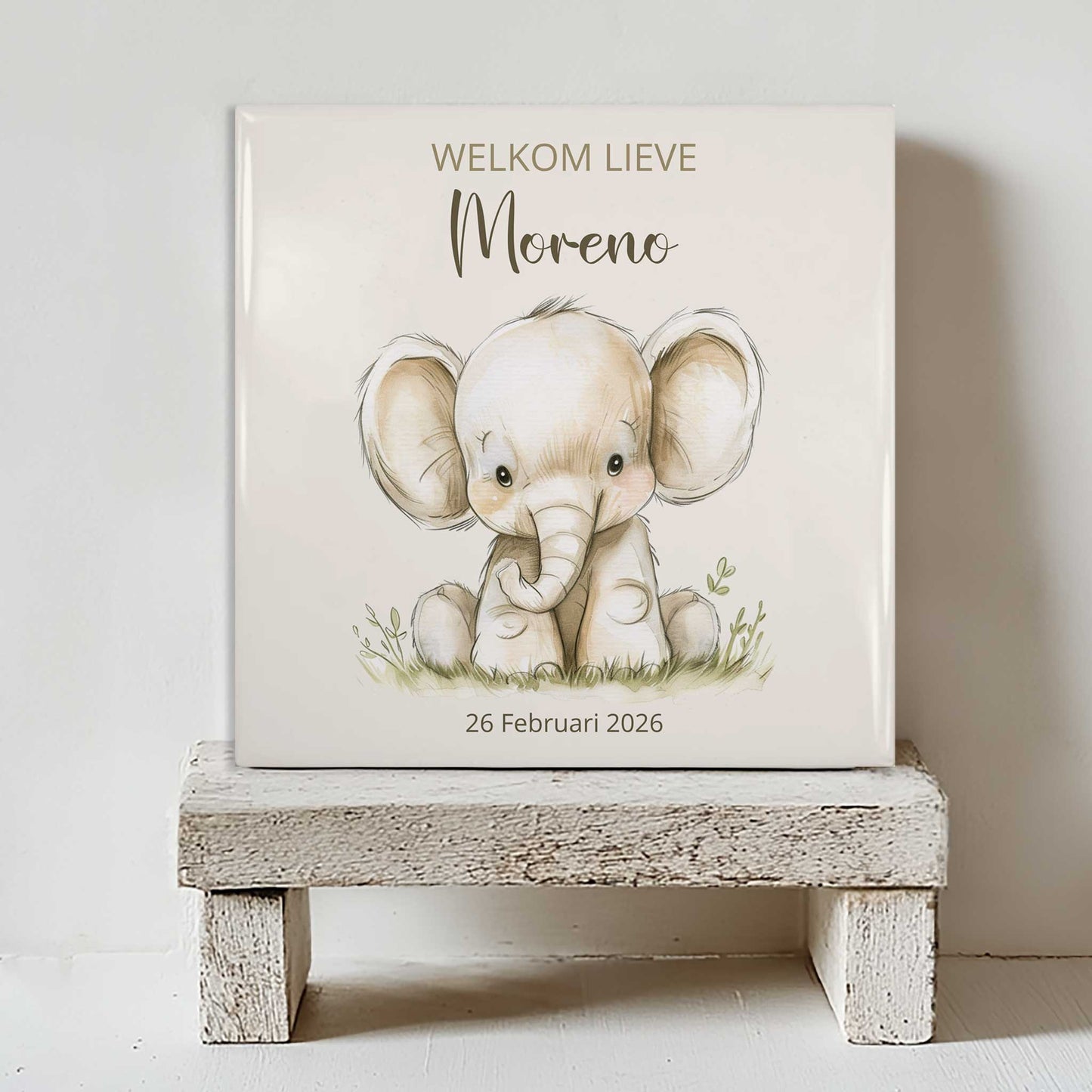 Keramisch tegeltje met een illustratie van een olifant, de tekst “welkom lieve Moreno” en de datum 26 februari 2026, geplaatst op een witte houten kruk
