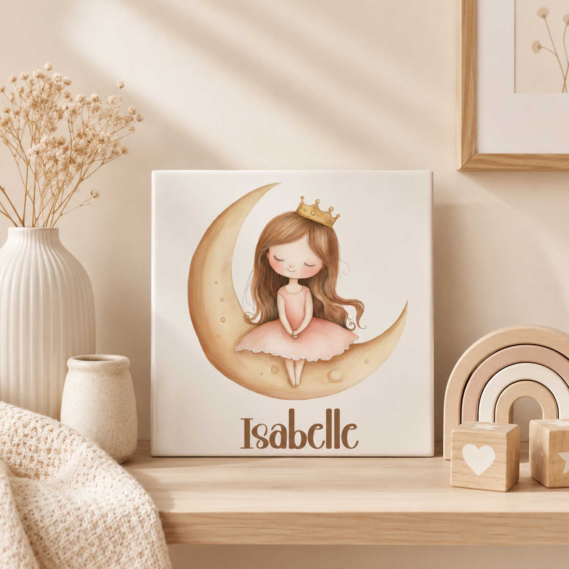 Keramisch prinsessen tegeltje met een prinses op een gouden maan en de naam Isabelle, geplaatst op een houten plank in een beige babykamer met droogbloemen en houten decoratie.