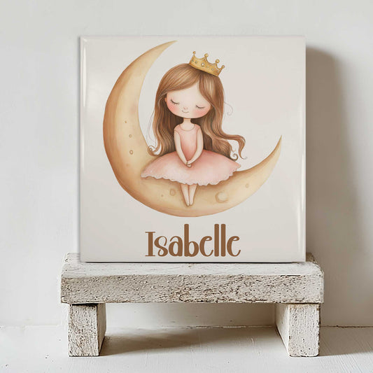 Keramisch prinsessen tegeltje met een prinses op een gouden maan en de naam Isabelle, geplaatst op een wit houten krukje tegen een lichte muur.