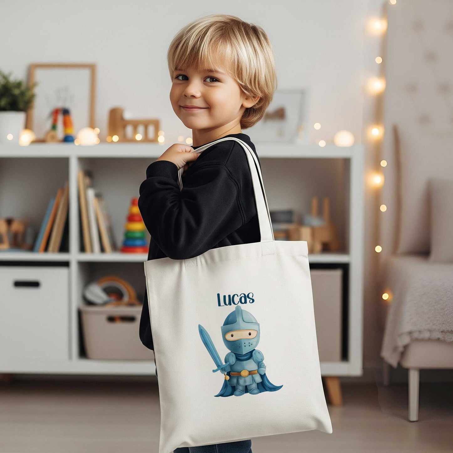 Jongen draagt een witte totebag met de naam Lucas en een illustratie van een blauwe ridder met een zwaard in een woonkamer.