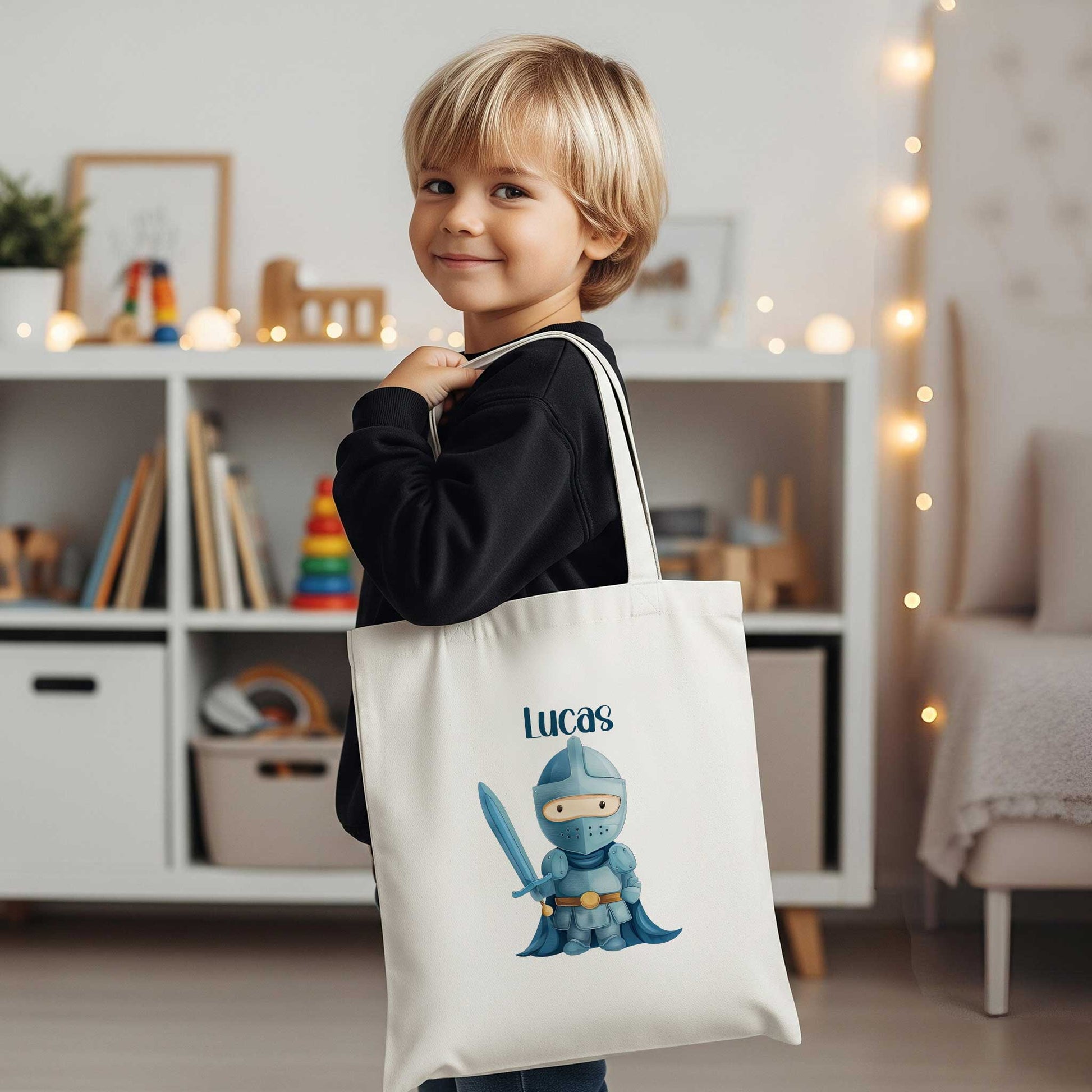 Jongen draagt een witte totebag met de naam Lucas en een illustratie van een blauwe ridder met een zwaard in een woonkamer.