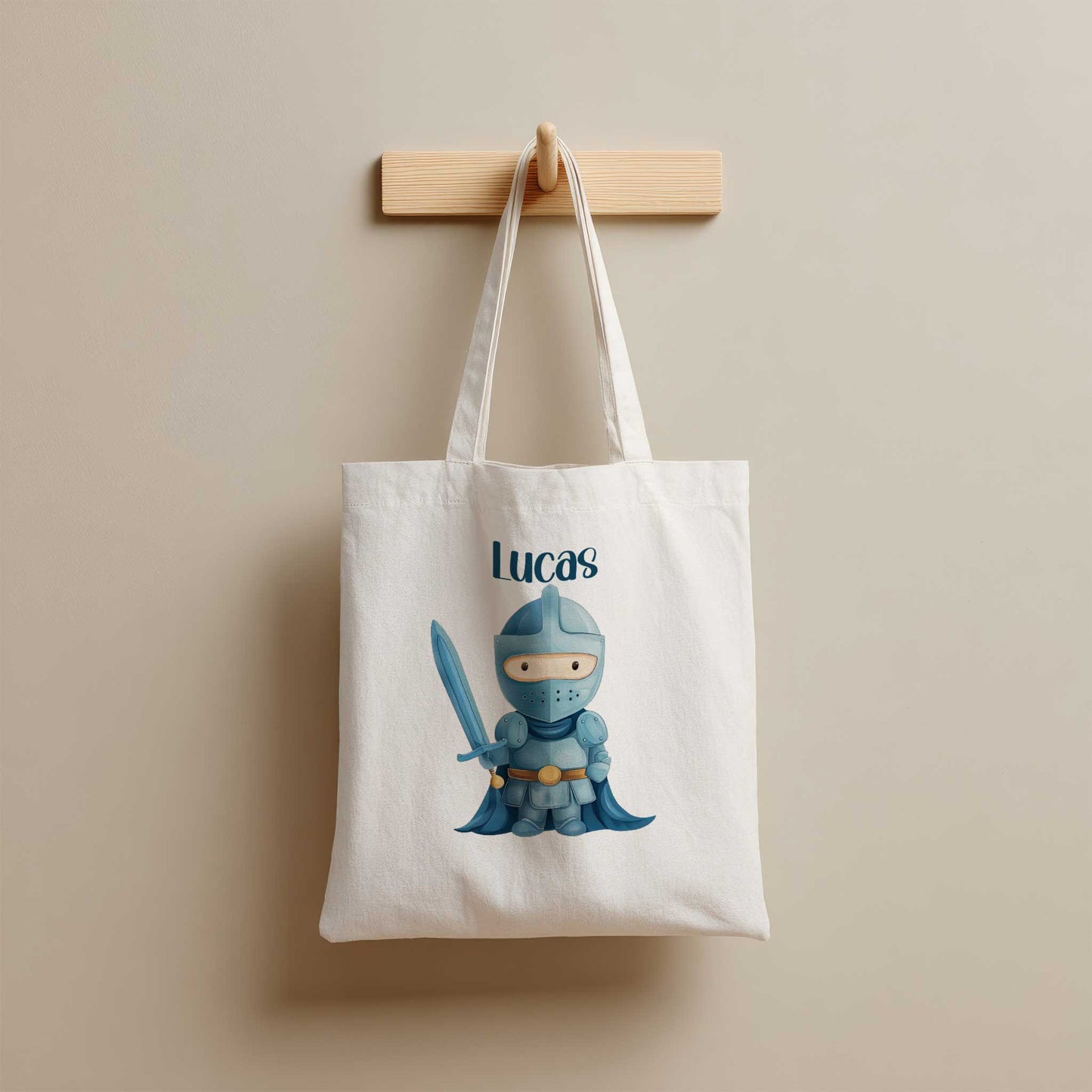 Witte totebag met de naam Lucas en een illustratie van een blauwe ridder met een zwaard, hangend aan een houten kapstok.