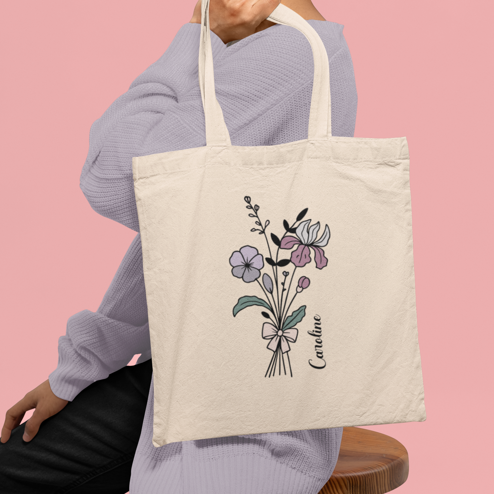 Totebag met bloemen lijntekening en naam Caroline, gedragen over schouder, roze achtergrond
