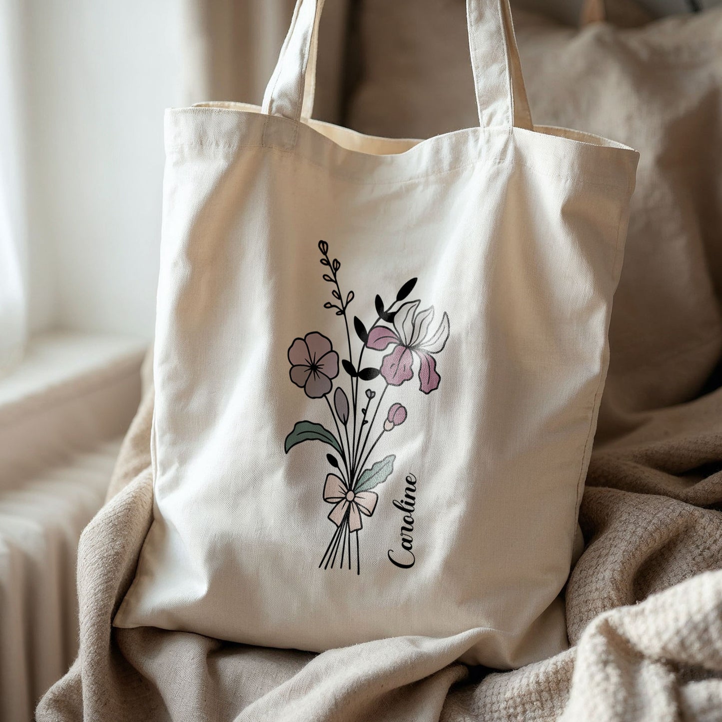 Totebag bloemen lijntekening en naam Caroline, gefotografeerd op bank bij raam met dekens.